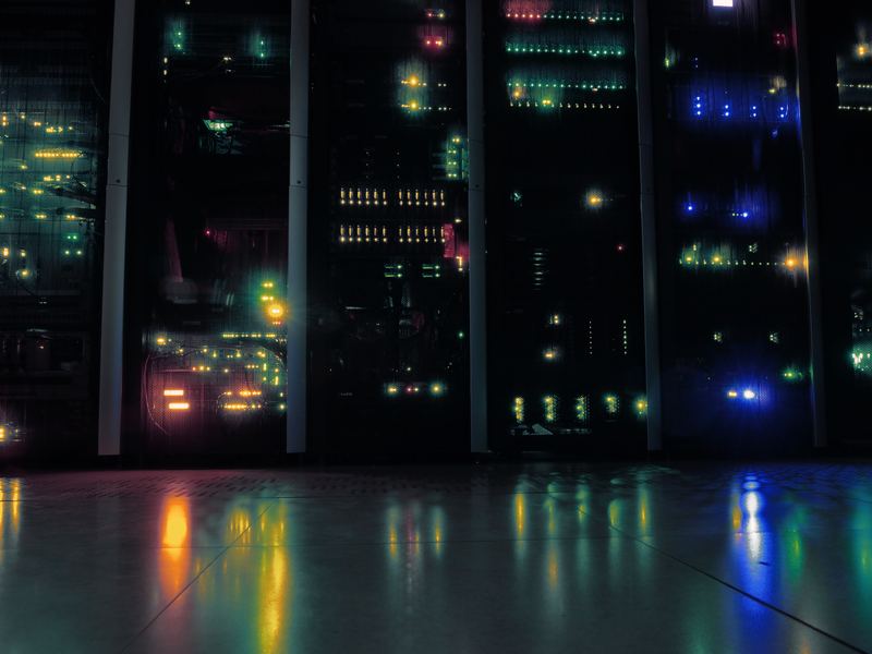 Rows of server racks in a dark data centre, their lights reflected in the floor.