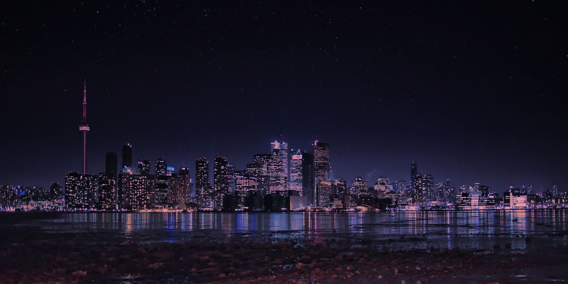 The Toronto skyline at night, seen across the water, with the CN Tower lit red under a sky full of stars.